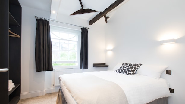 A bedroom with a bed, a wardrobe, a window with curtains, and a ceiling fan. - The Hurdwick (London)