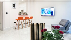 A modern living room with a grey sofa, a striped armchair, and a dining area with orange chairs. - The Hurdwick (London)
