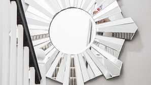 A staircase with a white railing, a white radiator, and a large, white, sunburst-shaped mirror on the wall. - The Hurdwick (London)