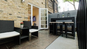 A patio area with wicker furniture, a table with lanterns, and a brick wall. - The Hurdwick (London)