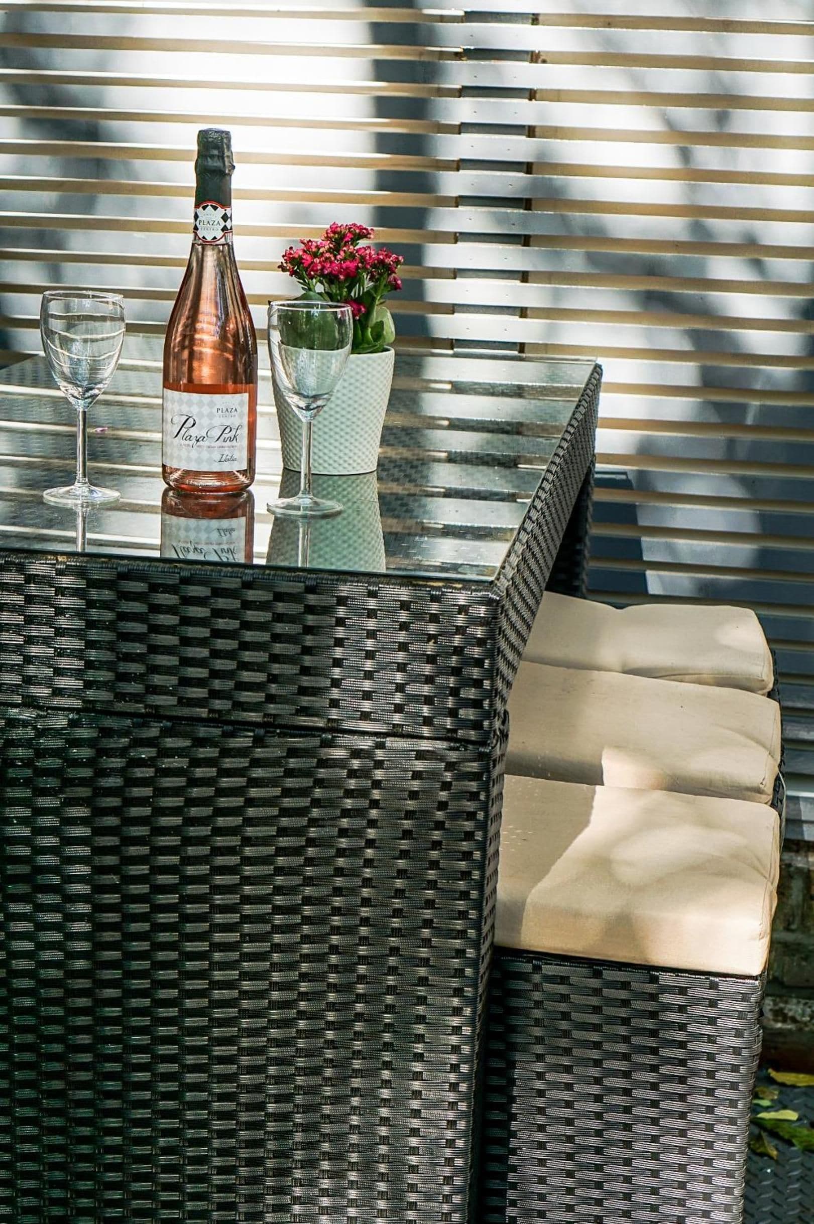 A wicker table with a bottle of wine, two glasses, and a vase with flowers.