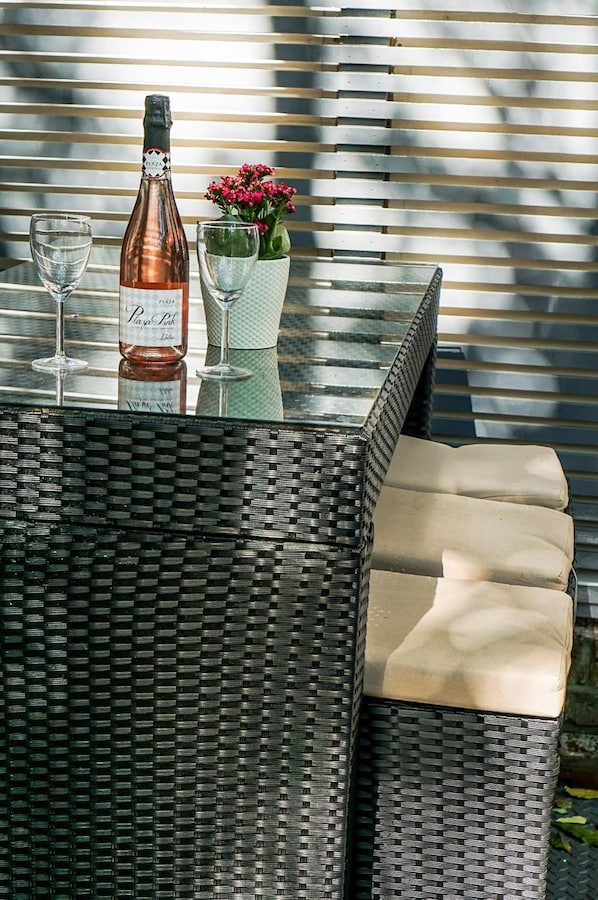 A wicker table with a bottle of wine, two glasses, and a vase with flowers. - The Hurdwick (London)