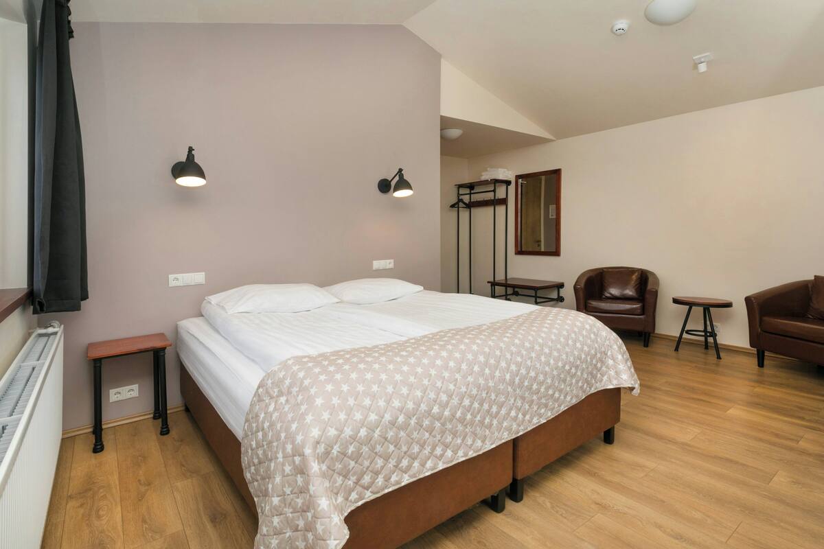 Un dormitorio con cama, mesitas de noche, una silla, una pequeña mesa y un espejo.