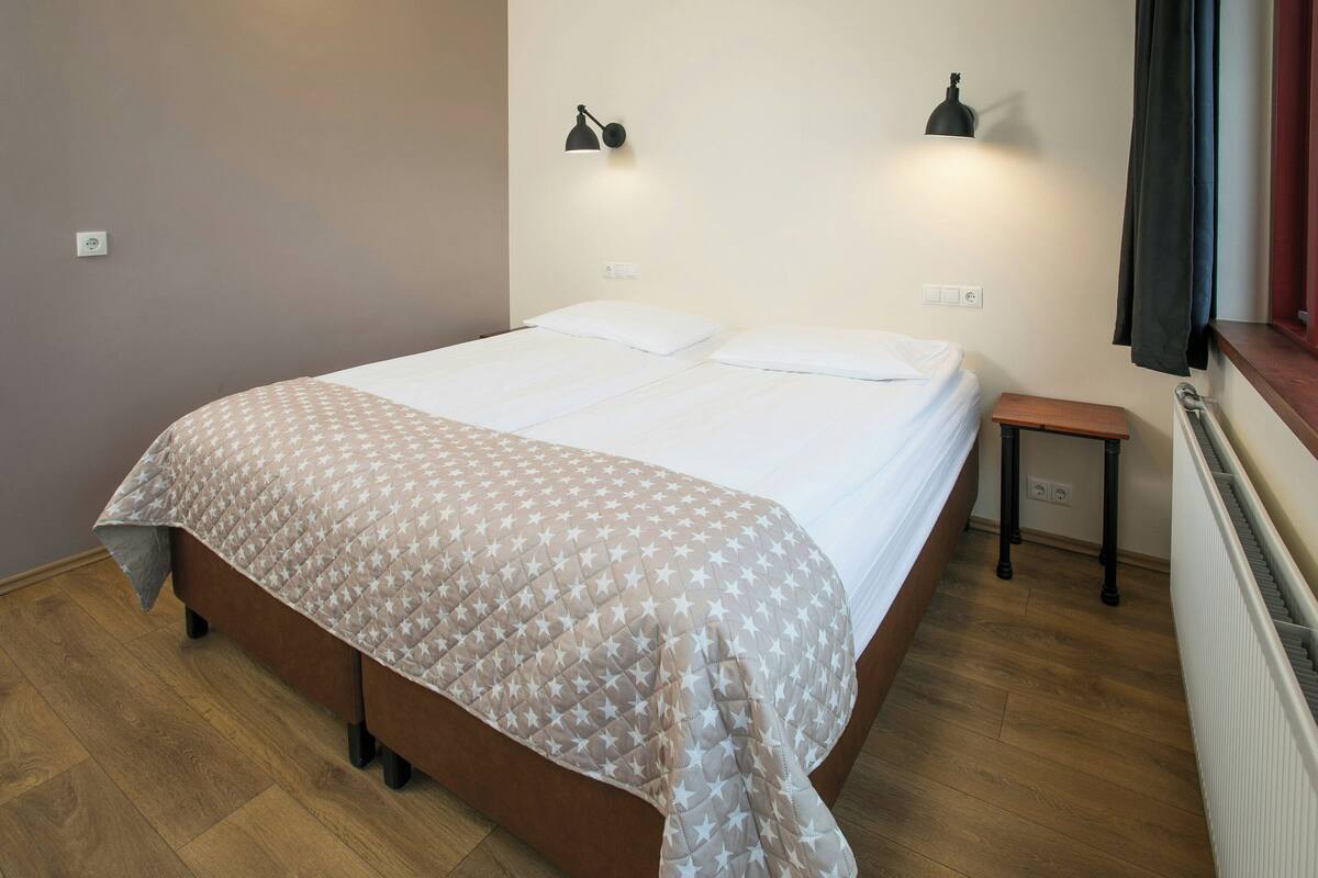 Un lit avec une couvre-lit à motifs, deux lampes de chevet, une petite table de chevet et une fenêtre avec des rideaux.
