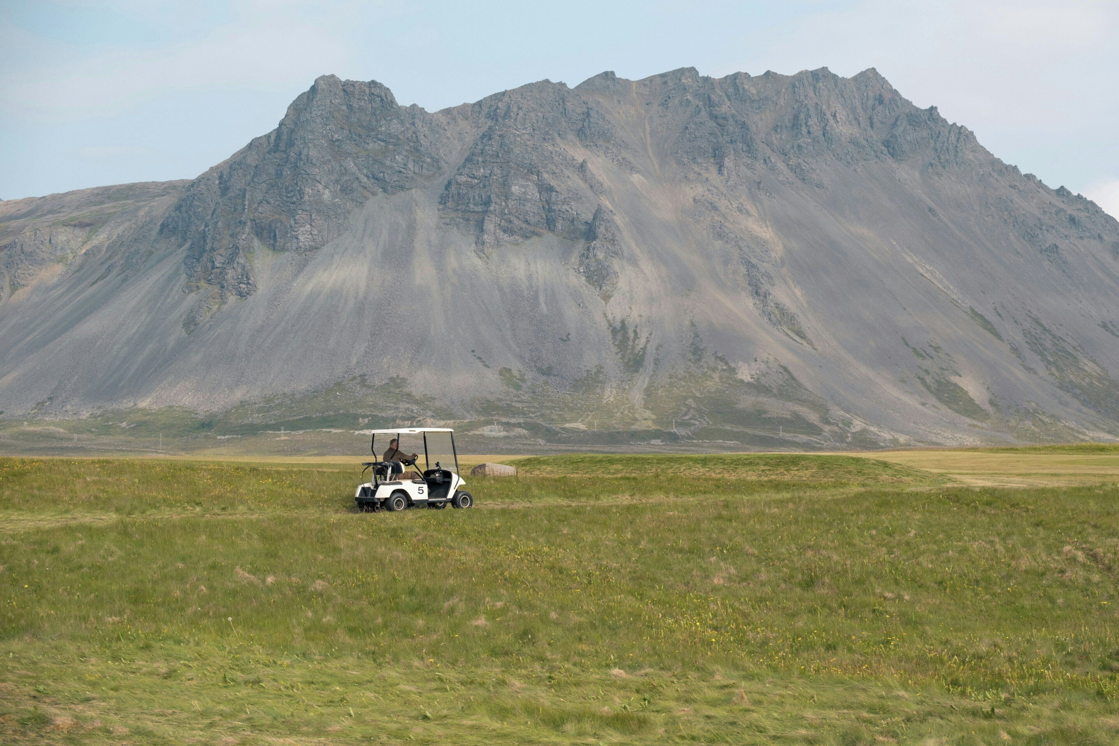 A golf cart on a grassy field with a mountain in the background.