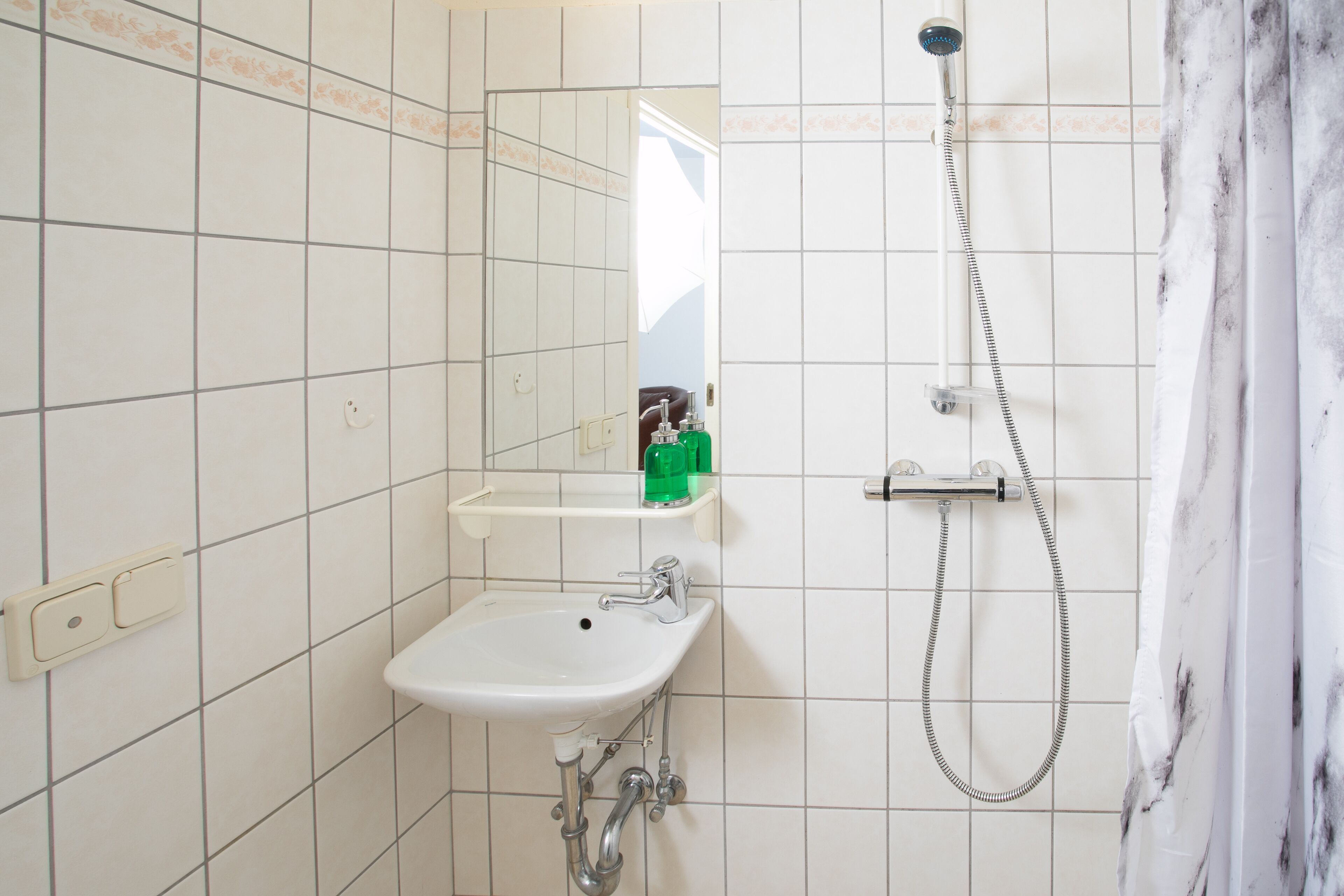 Un bagno con lavandino, specchio, doccia e uno scaffale con articoli da toilette.