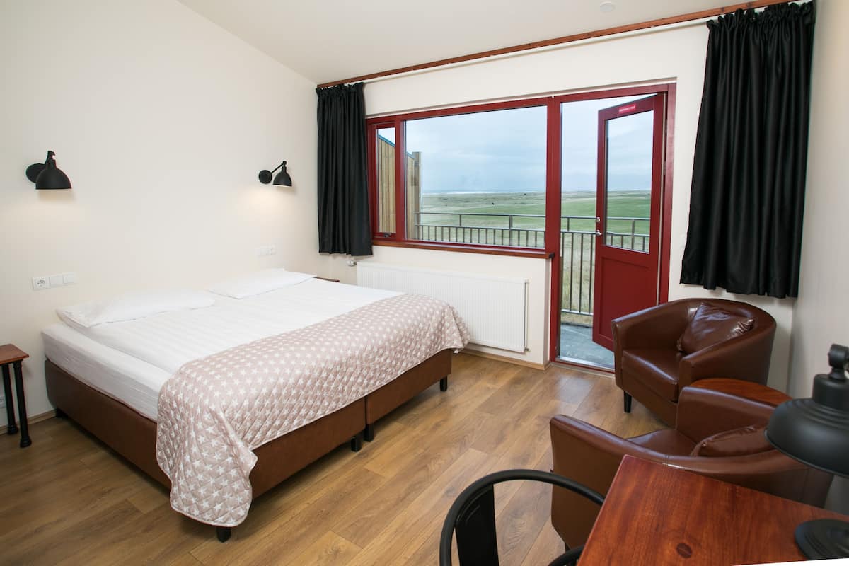Une chambre à coucher comprenant un lit, un bureau, une chaise et donnant sur l’extérieur par une porte.
