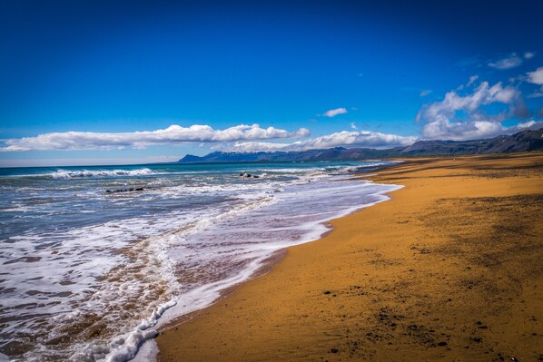 A beach with a clear sky, waves, and distant mountains.