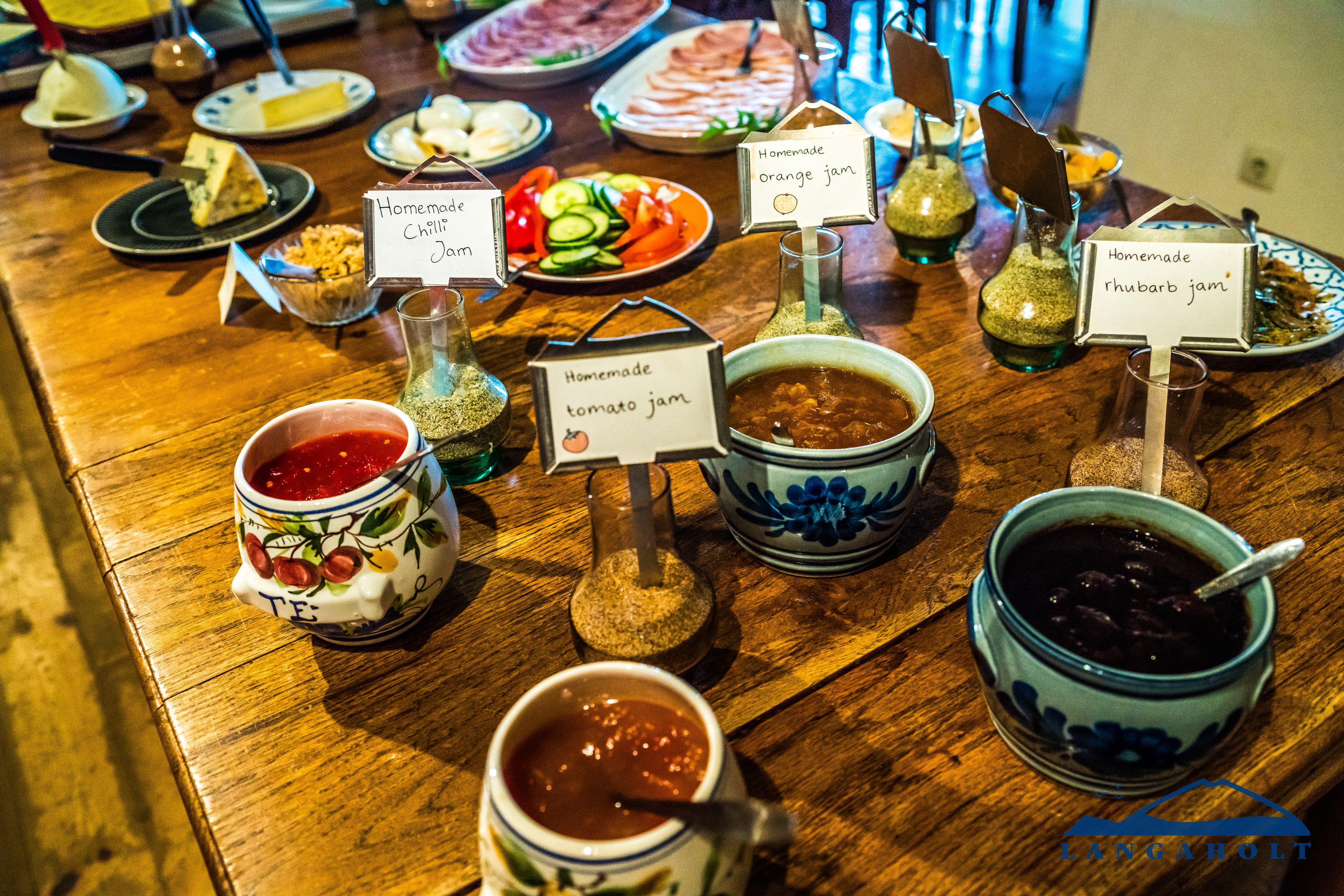 Une table où sont présentées différentes confitures et condiments faits maison, chacune étant étiquetée avec son nom.