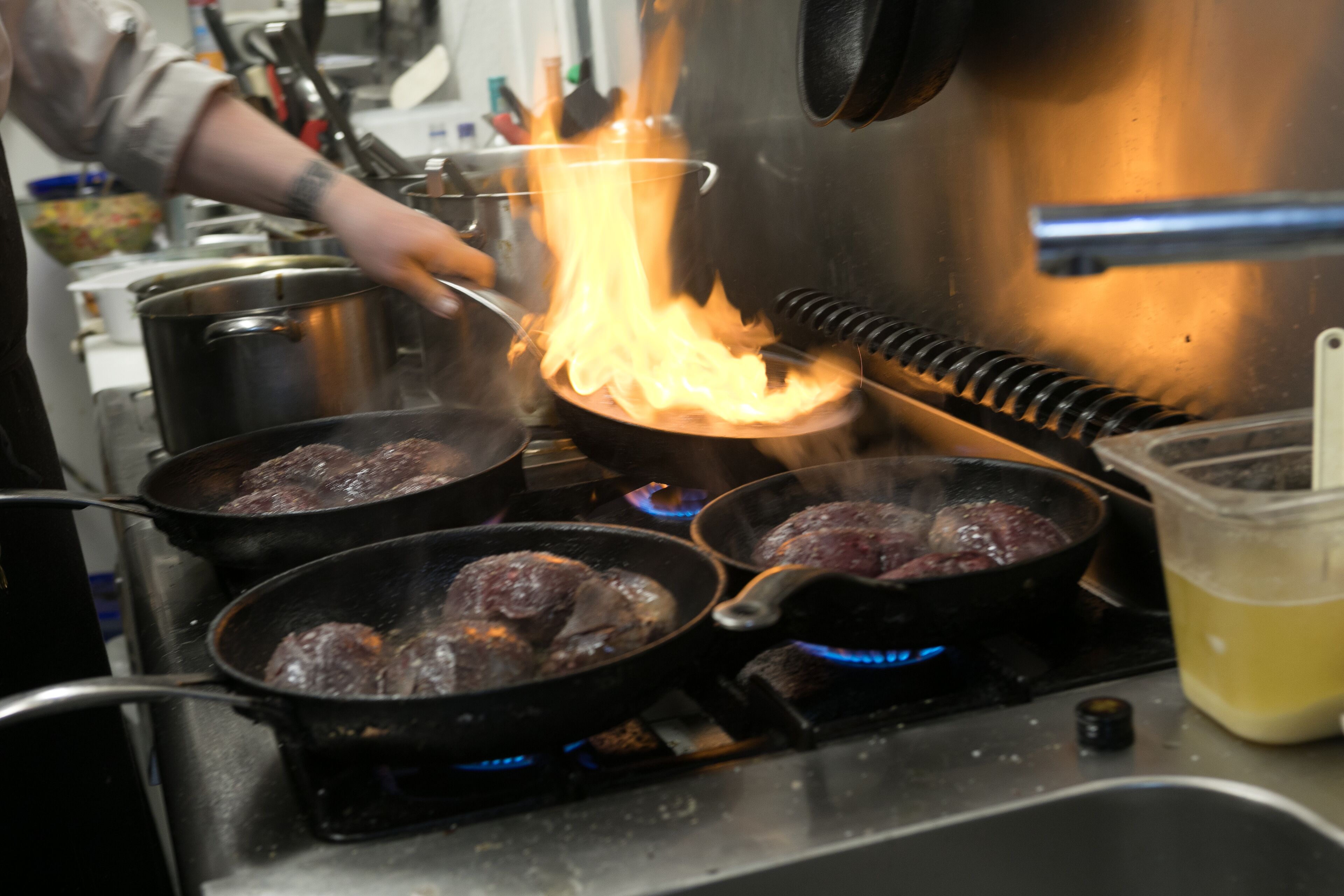 Une cuisine avec plusieurs poêles sur le feu, où l’on fait cuire de la viande.