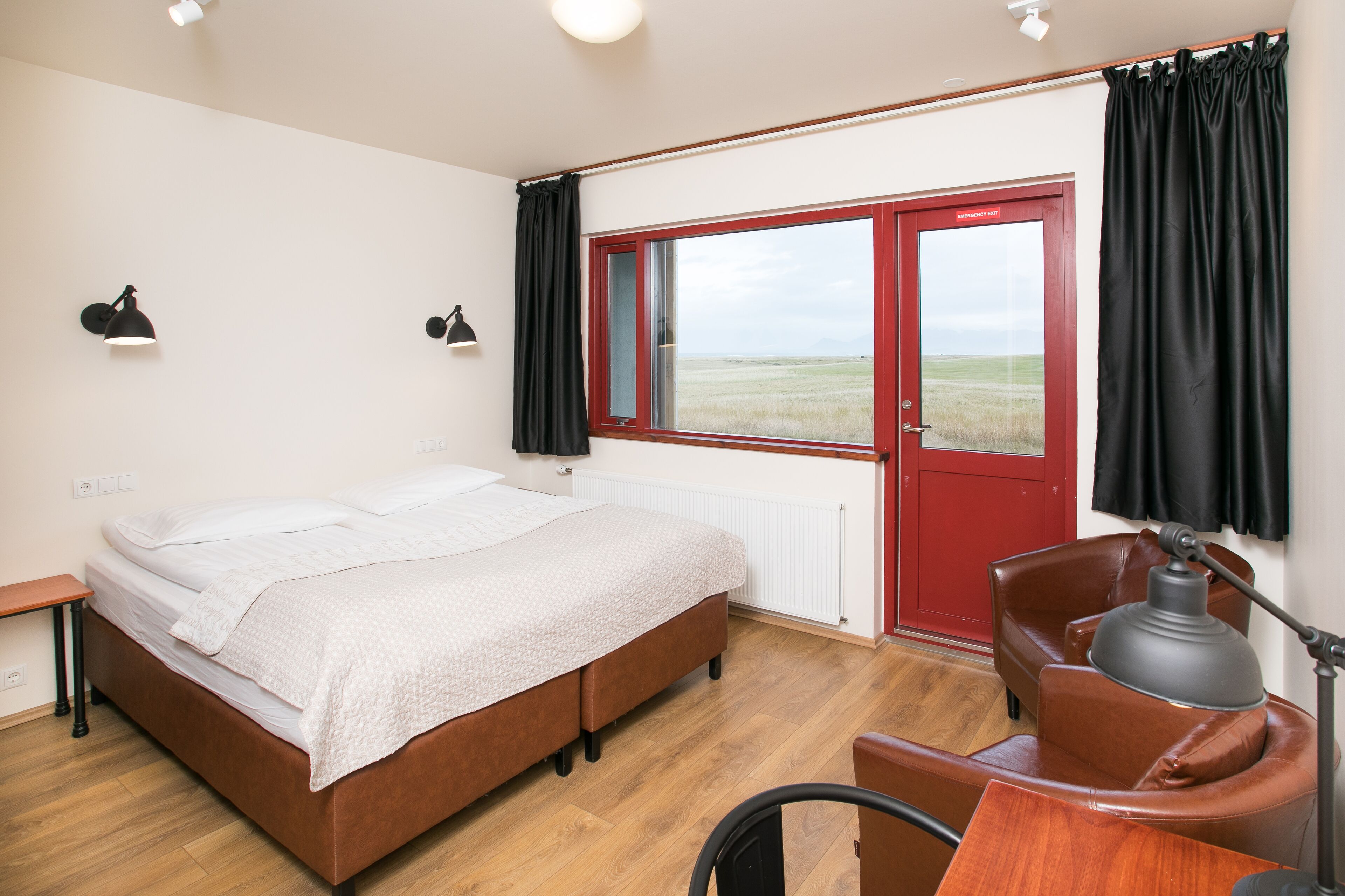 Un dormitorio con cama, escritorio, silla, ventana con cortinas y vistas al exterior.