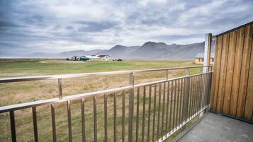 A balcony with a metal railing overlooking a grassy field and distant mountains.