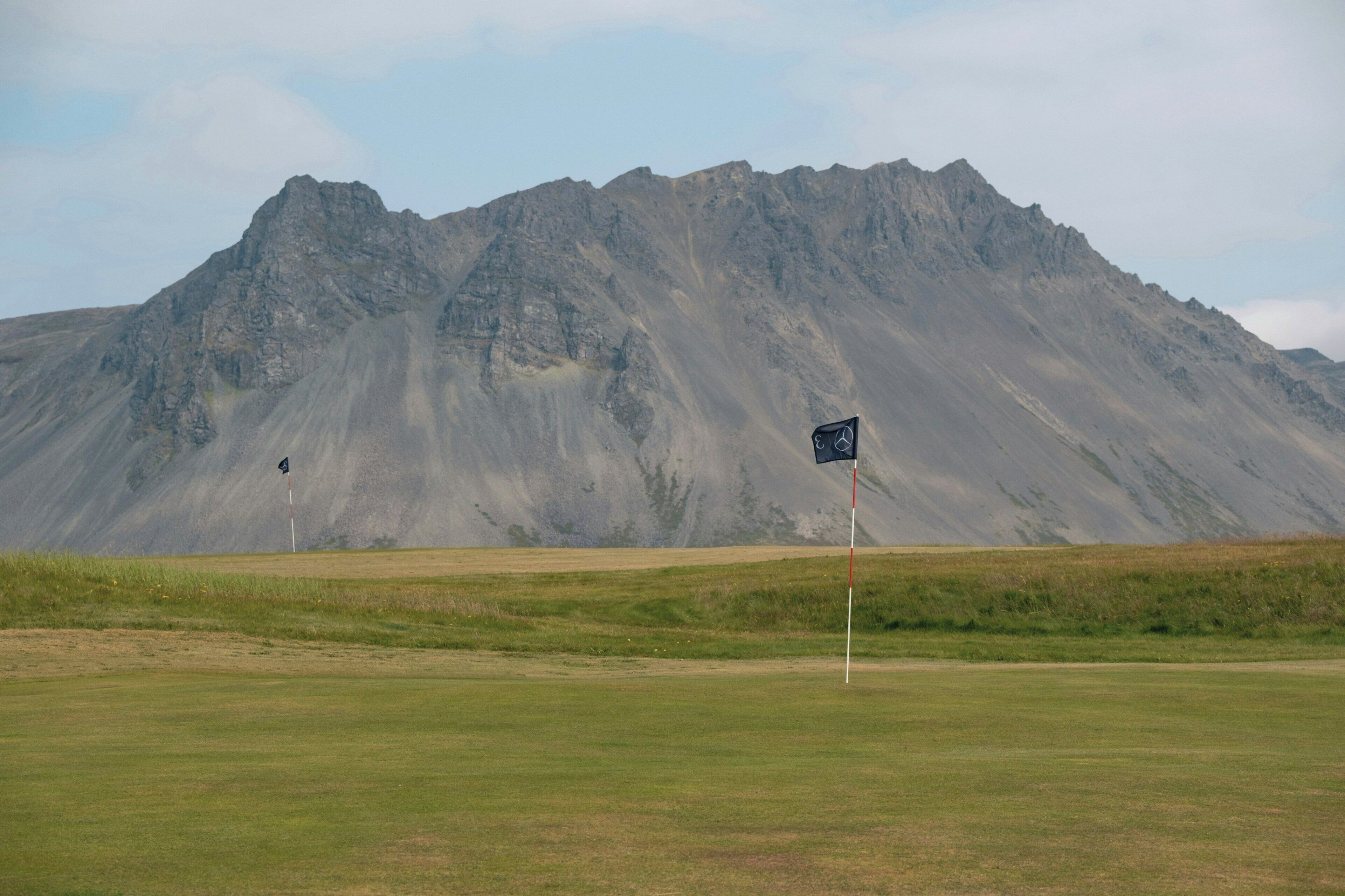 A golf course with a flagstick in the foreground and a mountain in the background.
