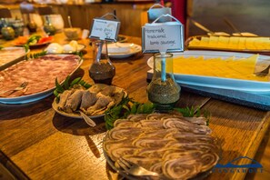 A buffet table with various food items including a tray of lamb pastrami, a dish of homemade traditional lamb sausage, and other assorted dishes.