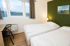 A room with two beds, a desk with a chair, a window with curtains, and a painting on the wall.