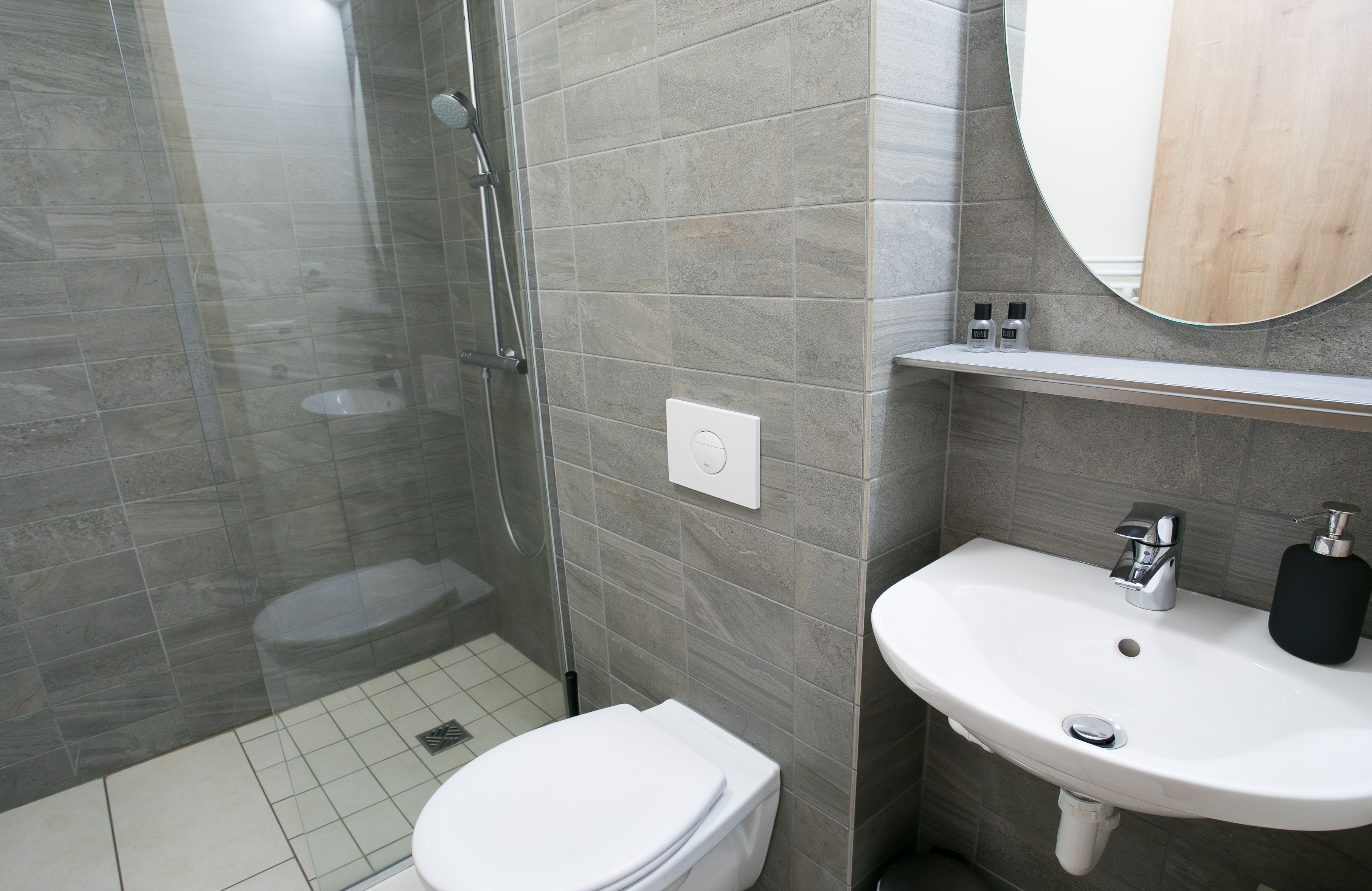 Un baño moderno con ducha de vidrio, inodoro blanco y lavamanos blanco con espejo arriba.