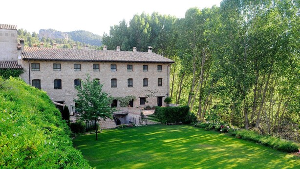 A stone building with a tiled roof, surrounded by lush greenery and trees. - Hotel Rural Font del Pas (Beceite)