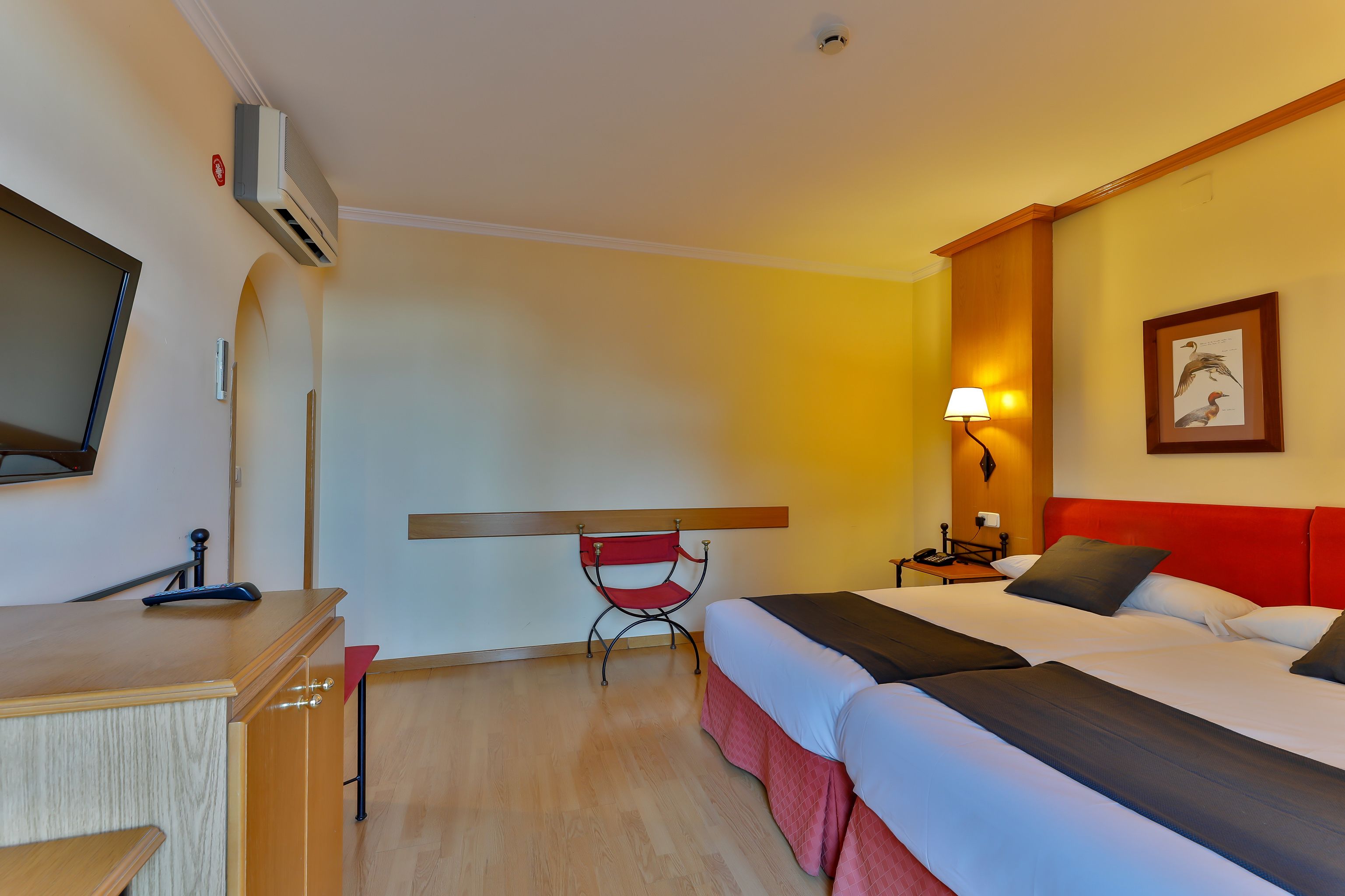 Habitación de hotel con dos camas, un escritorio, una silla, una lámpara y un cuadro en la pared.
