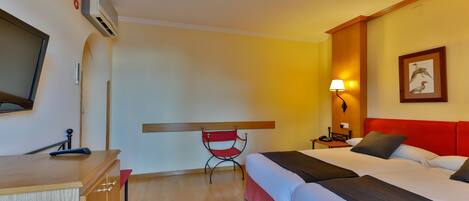 Habitación de hotel con dos camas, un escritorio, una silla, una lámpara y un cuadro en la pared.