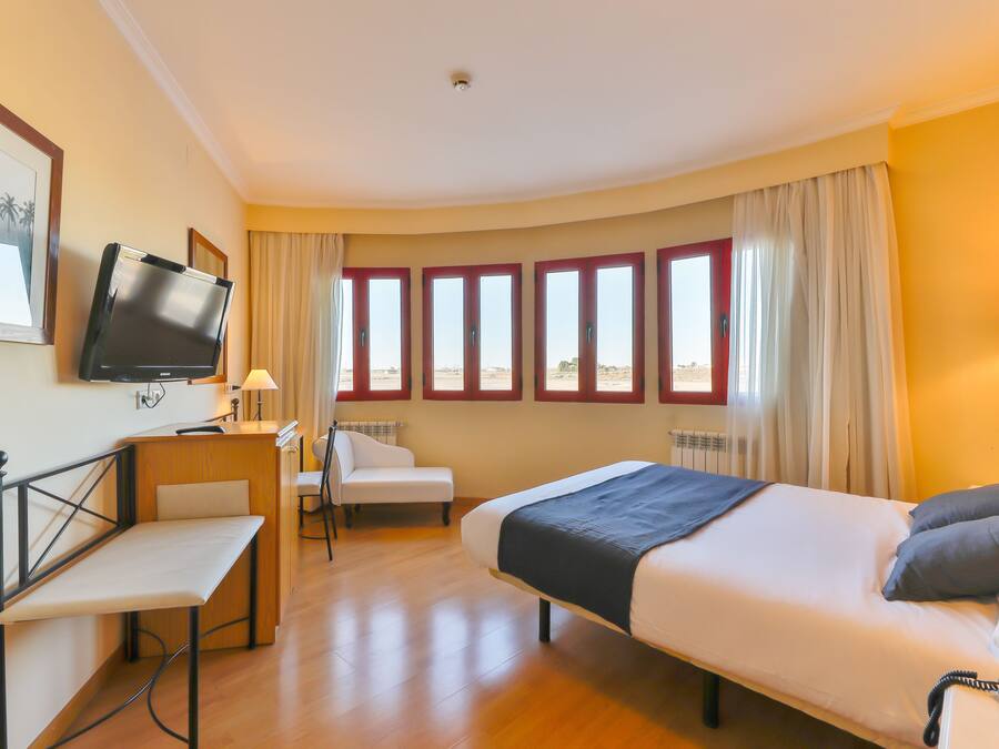 A hotel room with a bed, a desk, a chair, a television, and large windows.