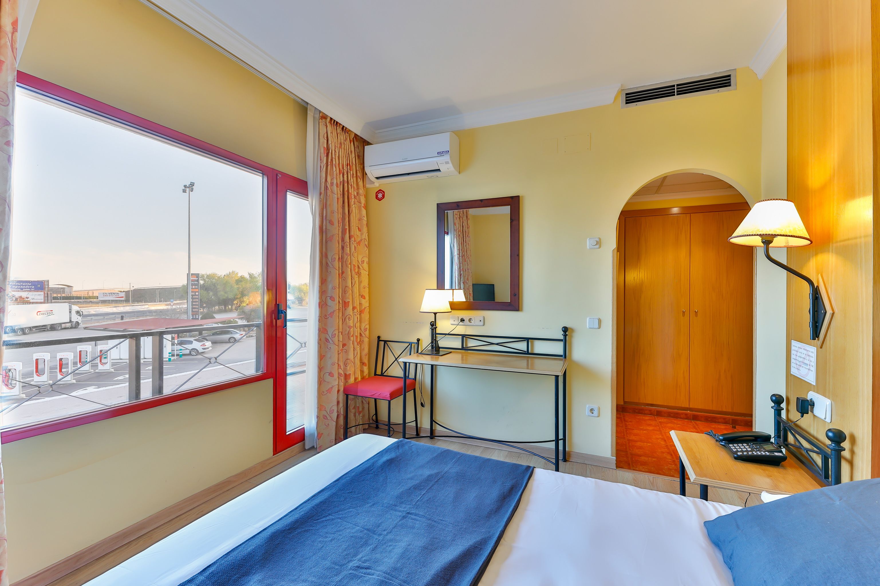 Habitación de hotel con cama, escritorio, silla y vistas al exterior.
