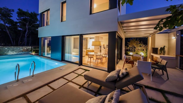 A modern house with a swimming pool, outdoor seating, and a well-lit interior. - Omega Villas Complex (Sutivan)