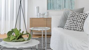 Une chambre d’hôtel moderne avec un lit blanc, un tapis à rayures noires et blanches, une table basse ronde, un lampadaire et un tableau au mur.