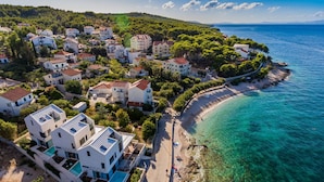 An aerial view of a coastal residential area with houses, a beach, and clear turquoise waters. - Omega Villas Complex (Sutivan)