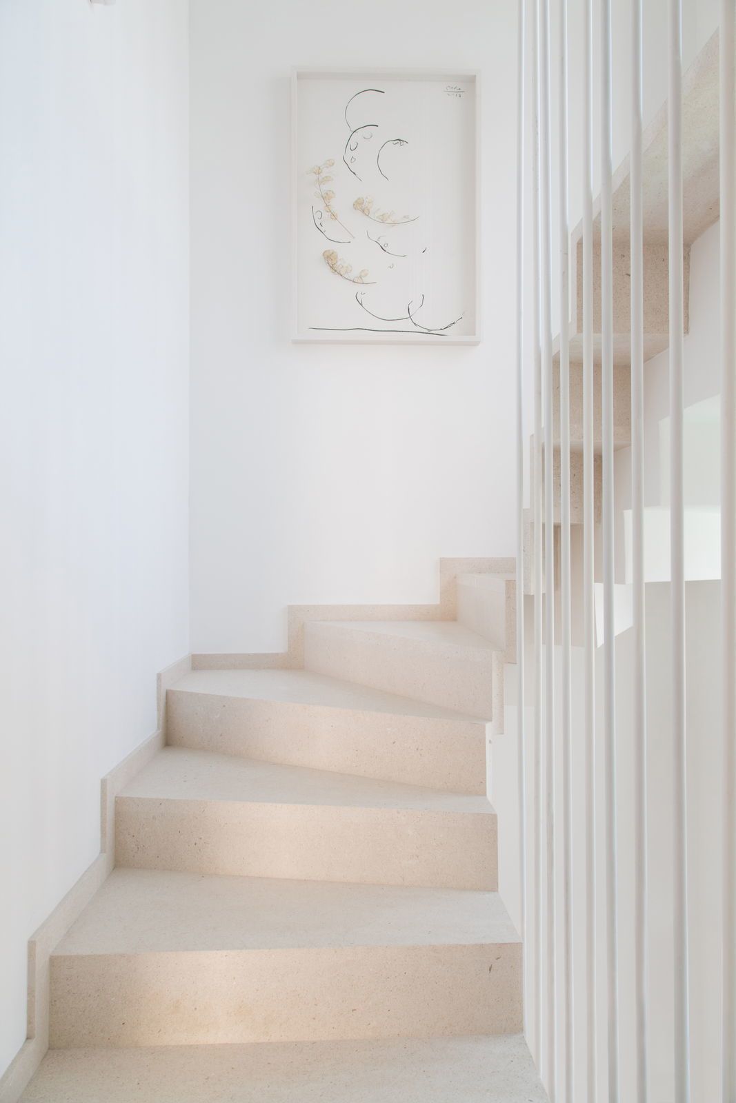 A staircase with a minimalist design, leading to a landing with a framed artwork.