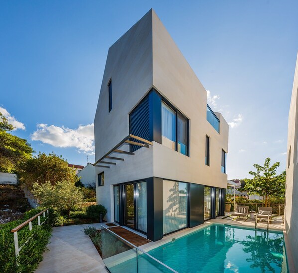 A modern two-story house with a swimming pool, large windows, and a staircase leading to the upper floor.