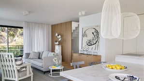 A modern living room with a grey sofa, white chairs, a dining table with plates of lemons, and a large window with curtains. - Omega Villas Complex (Sutivan)