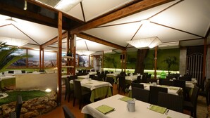 A restaurant with tables set for dining, a view of the city, and a tropical garden area. - Hotel Porta Rosa (Ascea)