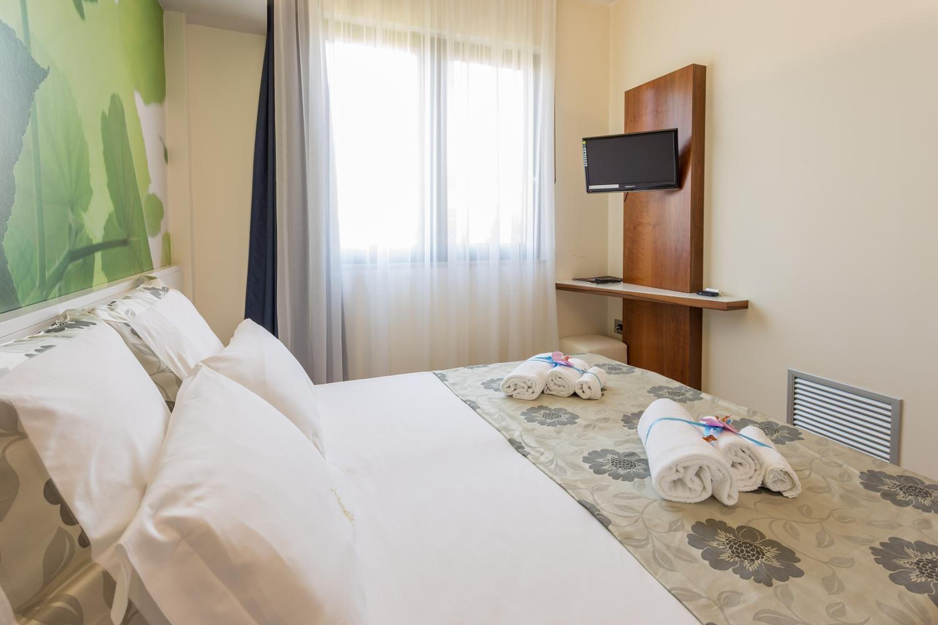 Ett hotellrum med en säng, en tv som är monterad på väggen och ett fönster med gardiner.