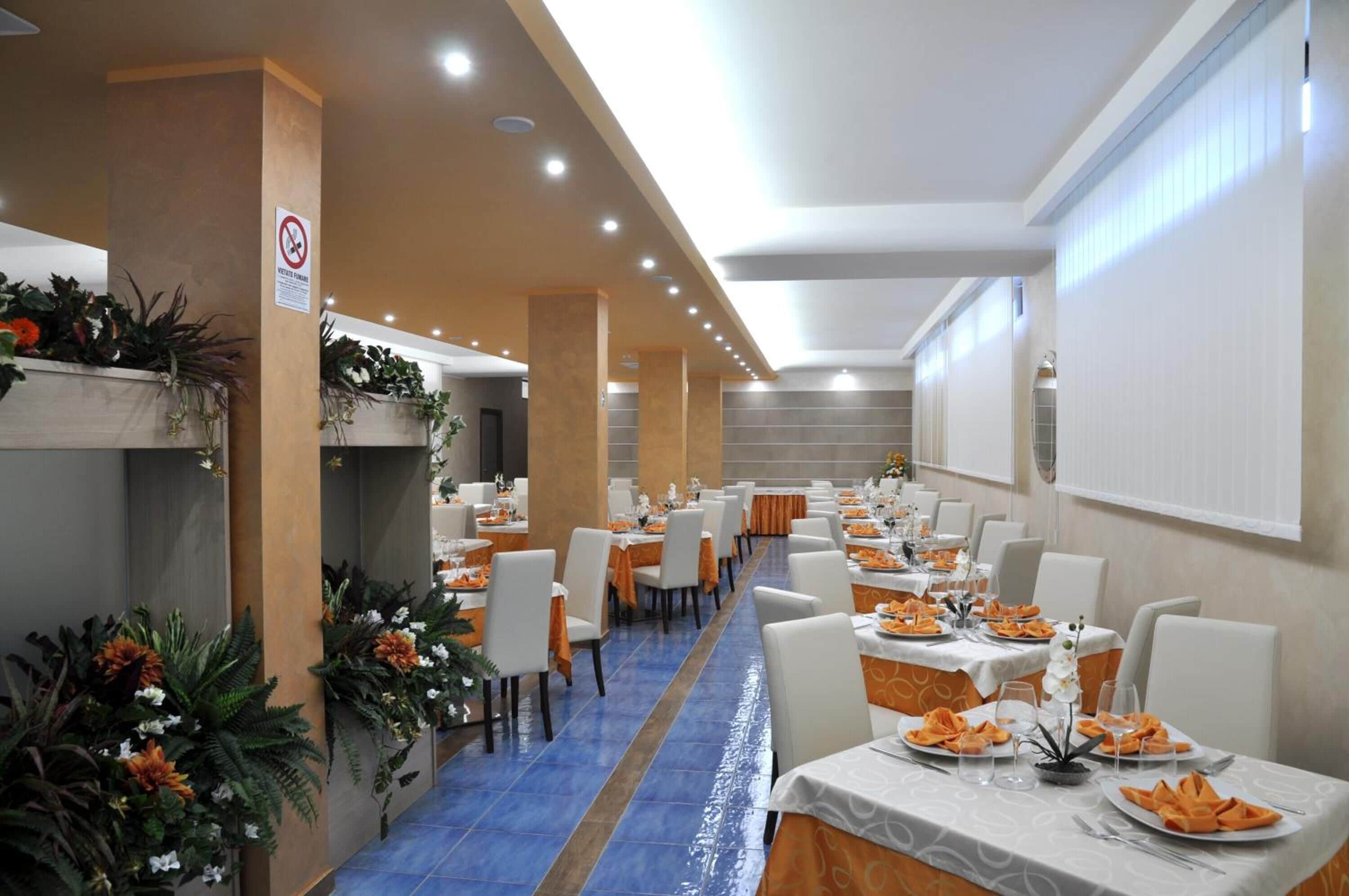 Un salón de banquetes con mesas largas, sillas blancas y manteles naranja.