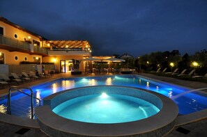 A swimming pool with a hot tub, lounge chairs, and a building with multiple balconies.