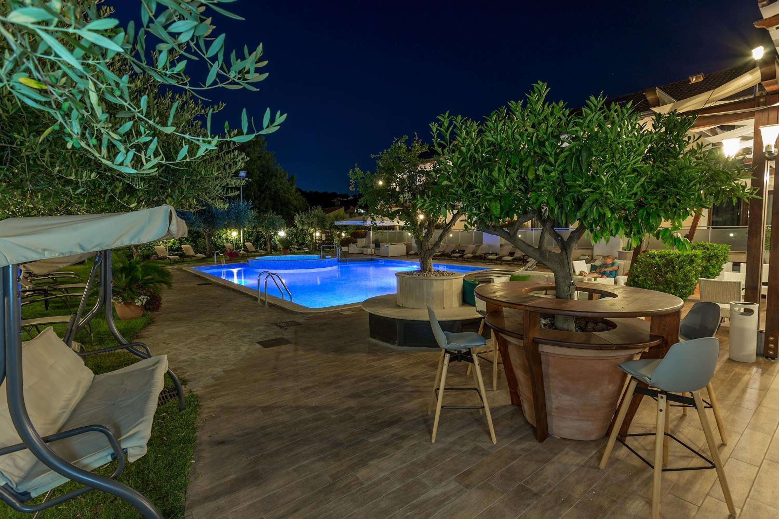 An outdoor pool area with lounge chairs and a table, surrounded by trees and plants.