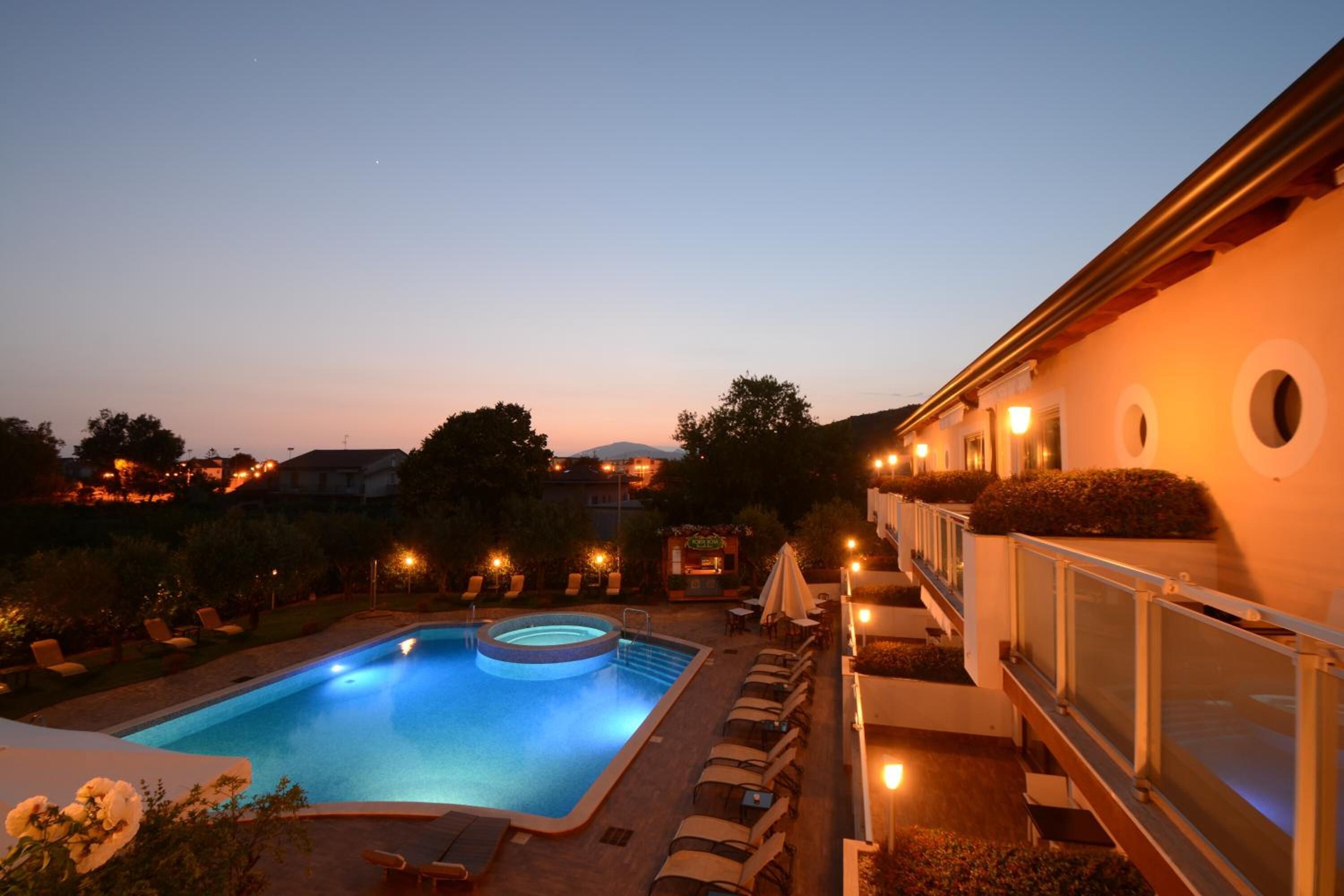 Ein Pool mit Liegestühlen und Bar, umgeben von einem angelegten Garten und einem Gebäude mit Balkon.