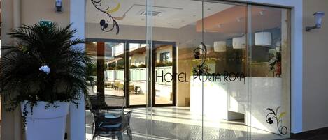 A hotel entrance with a glass door, a potted plant, and a seating area visible inside.