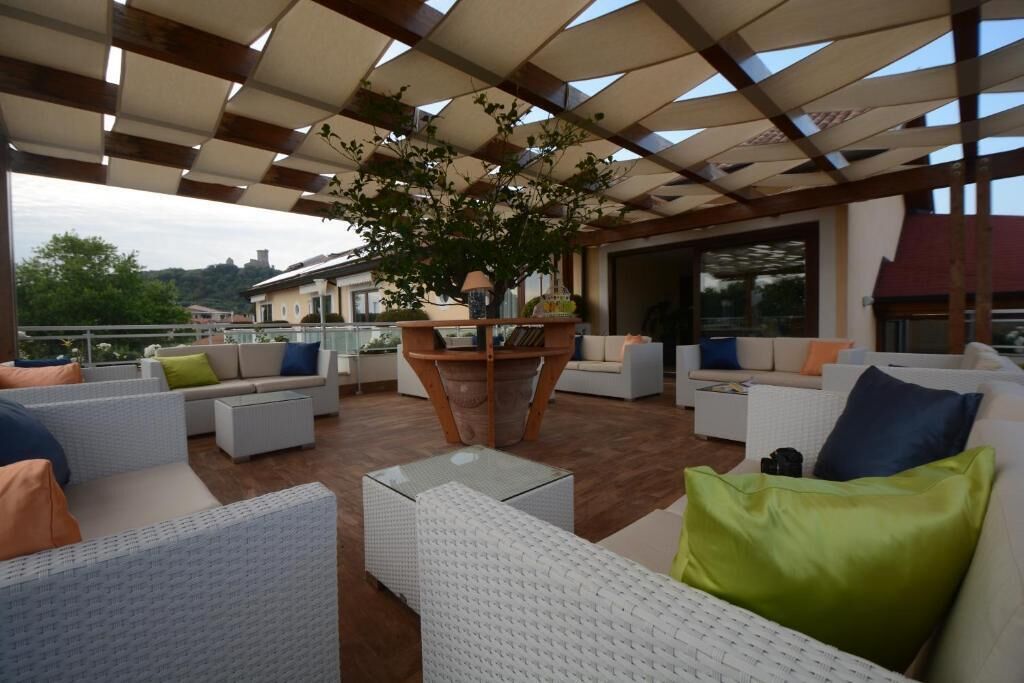 An outdoor patio area with white wicker furniture, green and blue cushions, and a central wooden table with a potted plant.