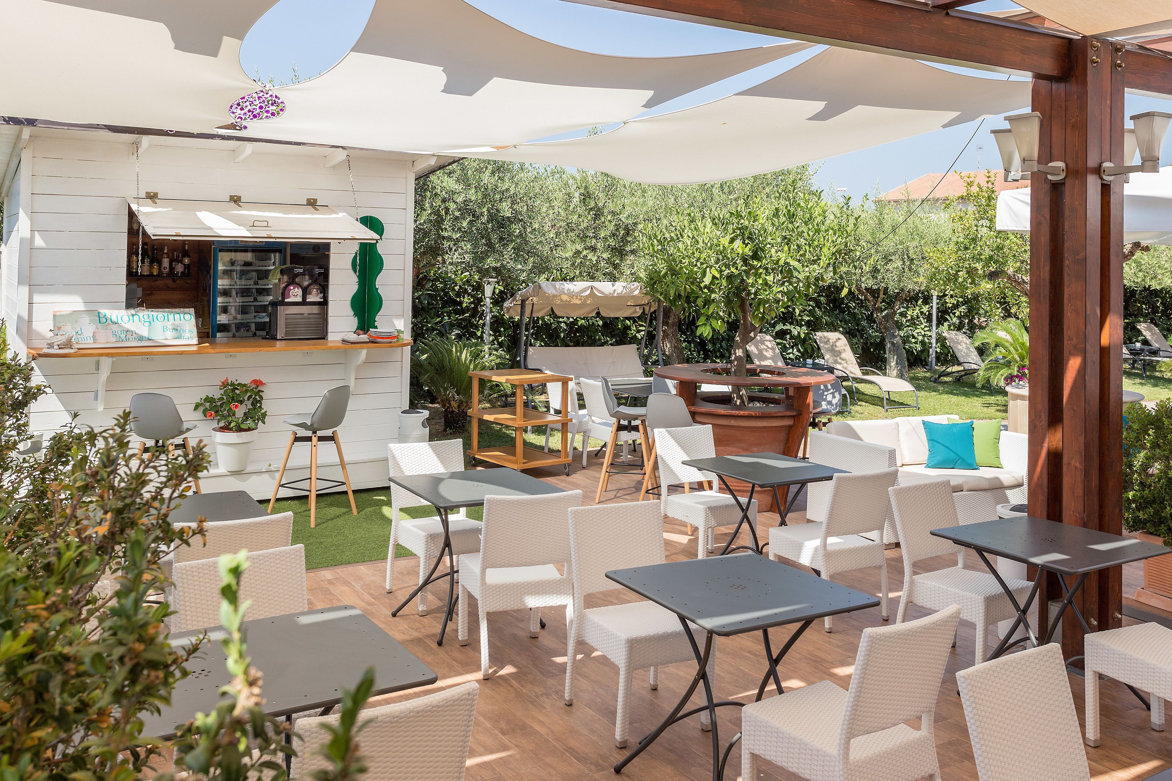 An outdoor patio with white wicker furniture, a bar area, and a view of a garden.