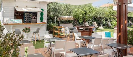 Un patio al aire libre con mobiliario de mimbre blanco, una zona de bar y vistas a un jardín.