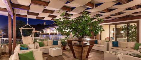 A rooftop lounge with outdoor seating, a hanging chair, and a central plant.