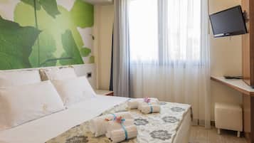 Habitación de hotel con una cama grande, un escritorio, un televisor y una ventana con cortinas translúcidas.