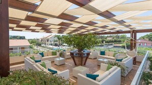 A covered outdoor seating area with wicker furniture, a central round table, and a view of the surrounding landscape. - Hotel Porta Rosa (Ascea)