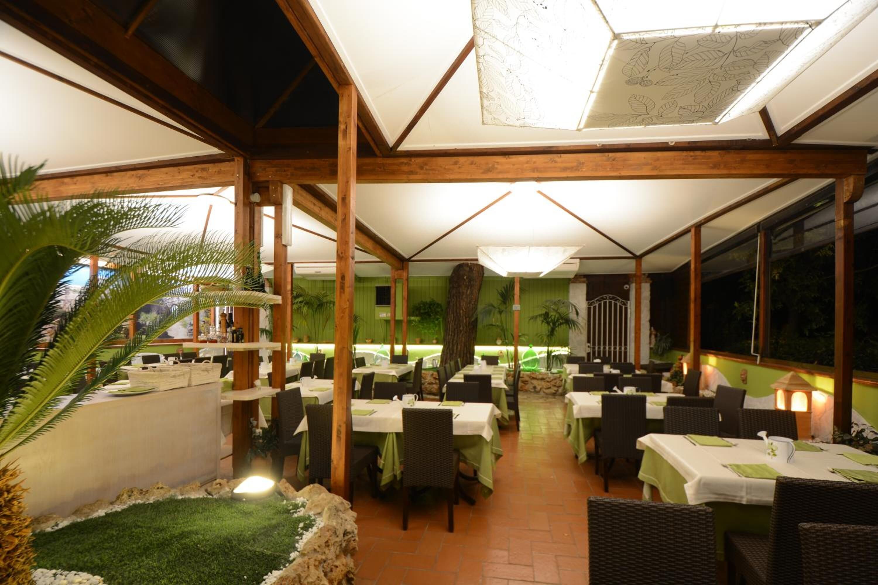 An indoor dining area with wooden beams, tables with green tablecloths, and a view of the outdoors.