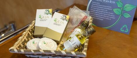 A basket containing OLIJA shower cassettes, a bottle of oil, and a card for Hotel Porta Rosa.