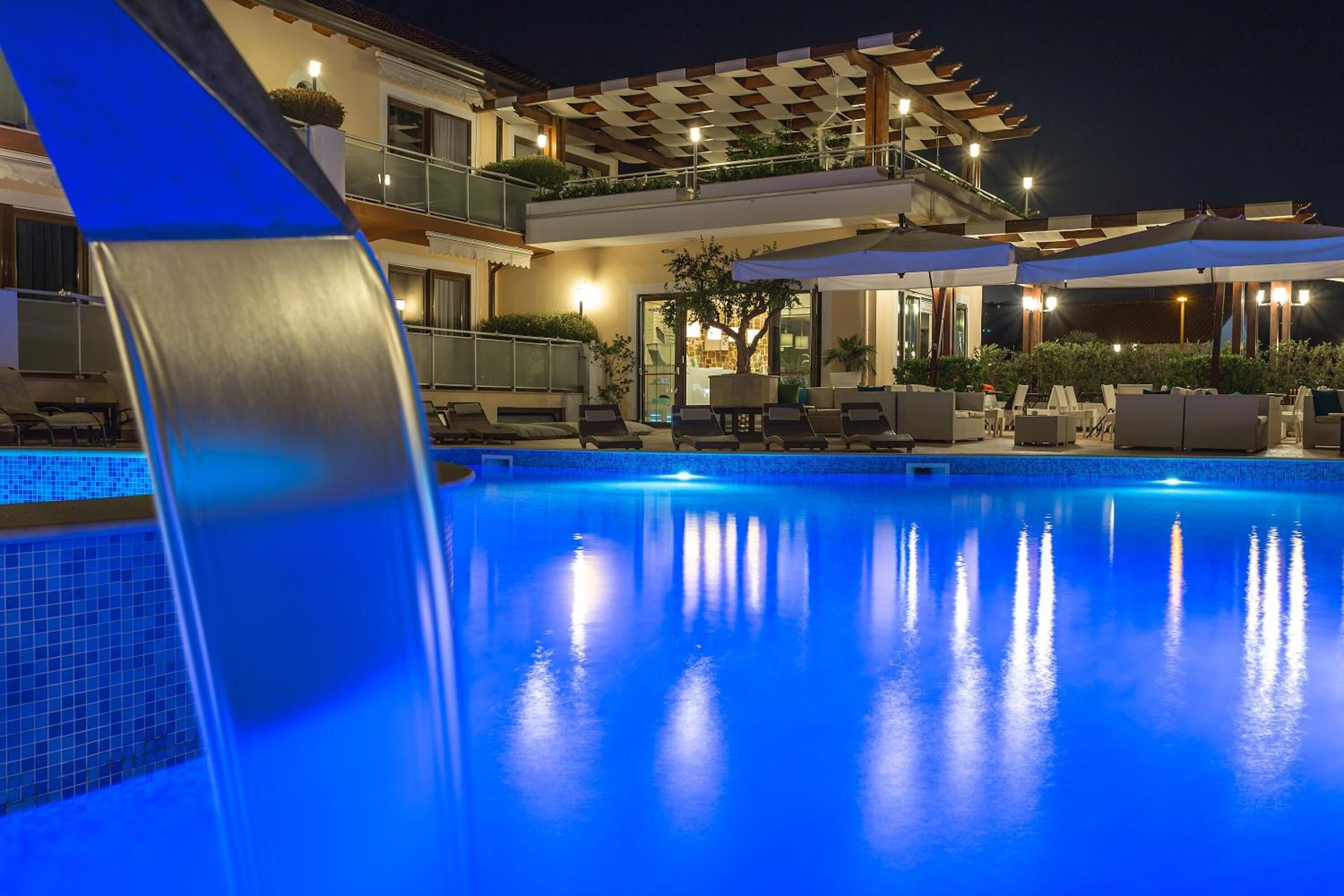 A poolside area with lounge chairs and umbrellas, a covered seating area, and a building with balconies.