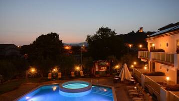 Una piscina con jacuzzi, rodeada de sillones de descanso y un restaurante.