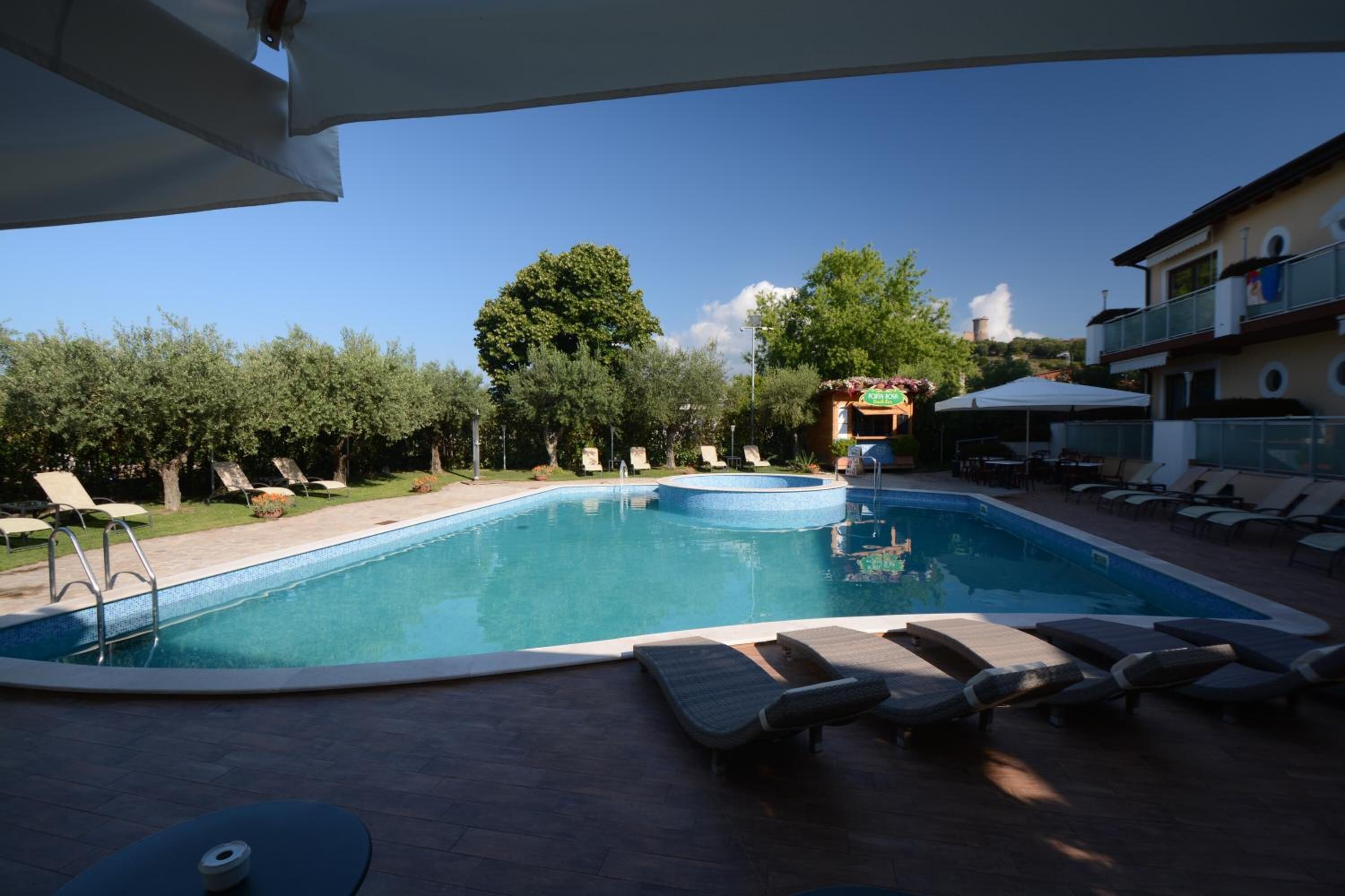 Ein Swimmingpool mit Liegestühlen und einem Whirlpool, umgeben von Bäumen und Gebäuden.