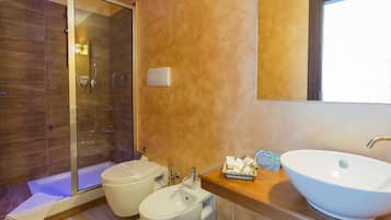 Une salle de bain moderne dotée d’une douche à parois de verre, d’un bidet et d’un grand lavabo sur pied.
